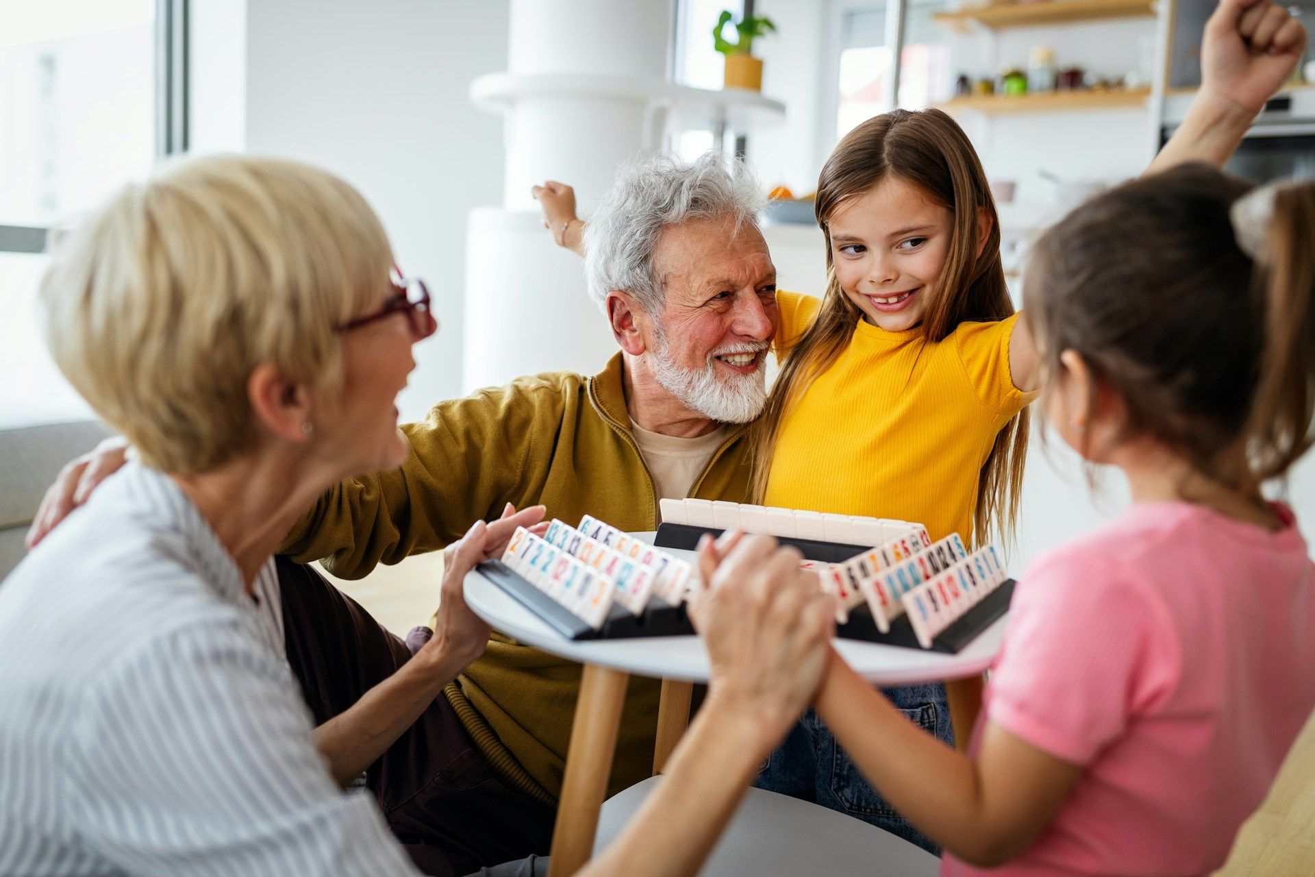 Grandparents and granddaughters playing a board game, smiling and celebrating.
