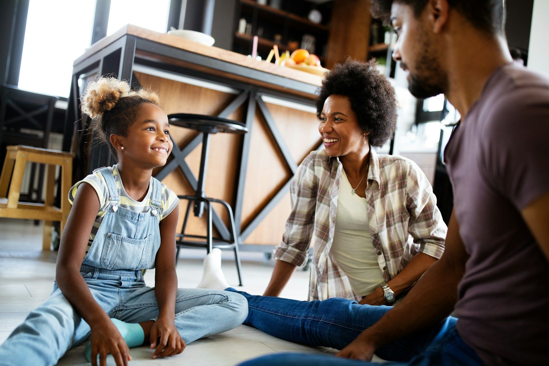 Family of three smiling while sitting on the floor indoors.