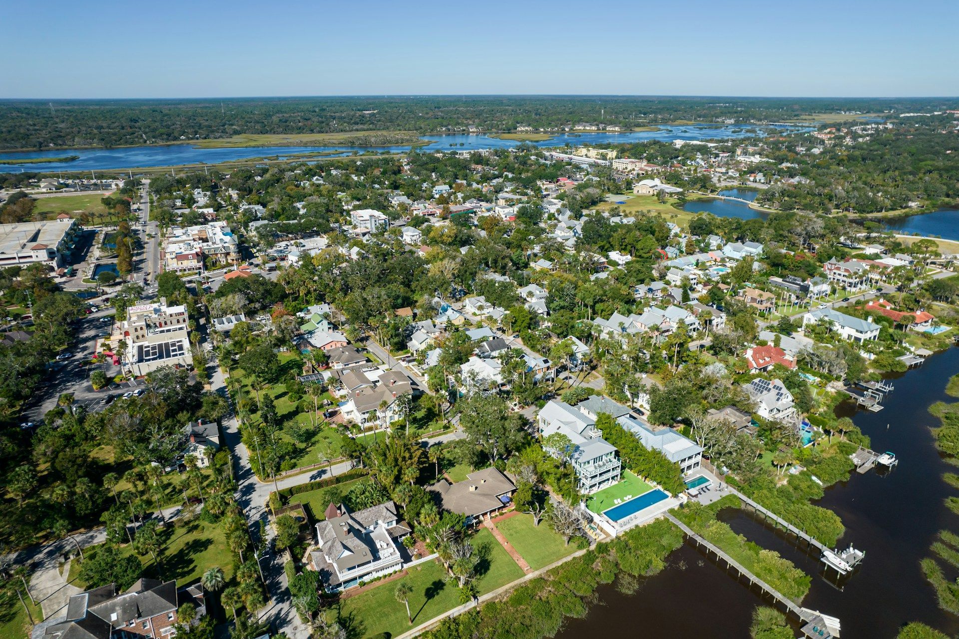 Aerial view of a coastal town with houses, trees, and waterways under a clear sky.