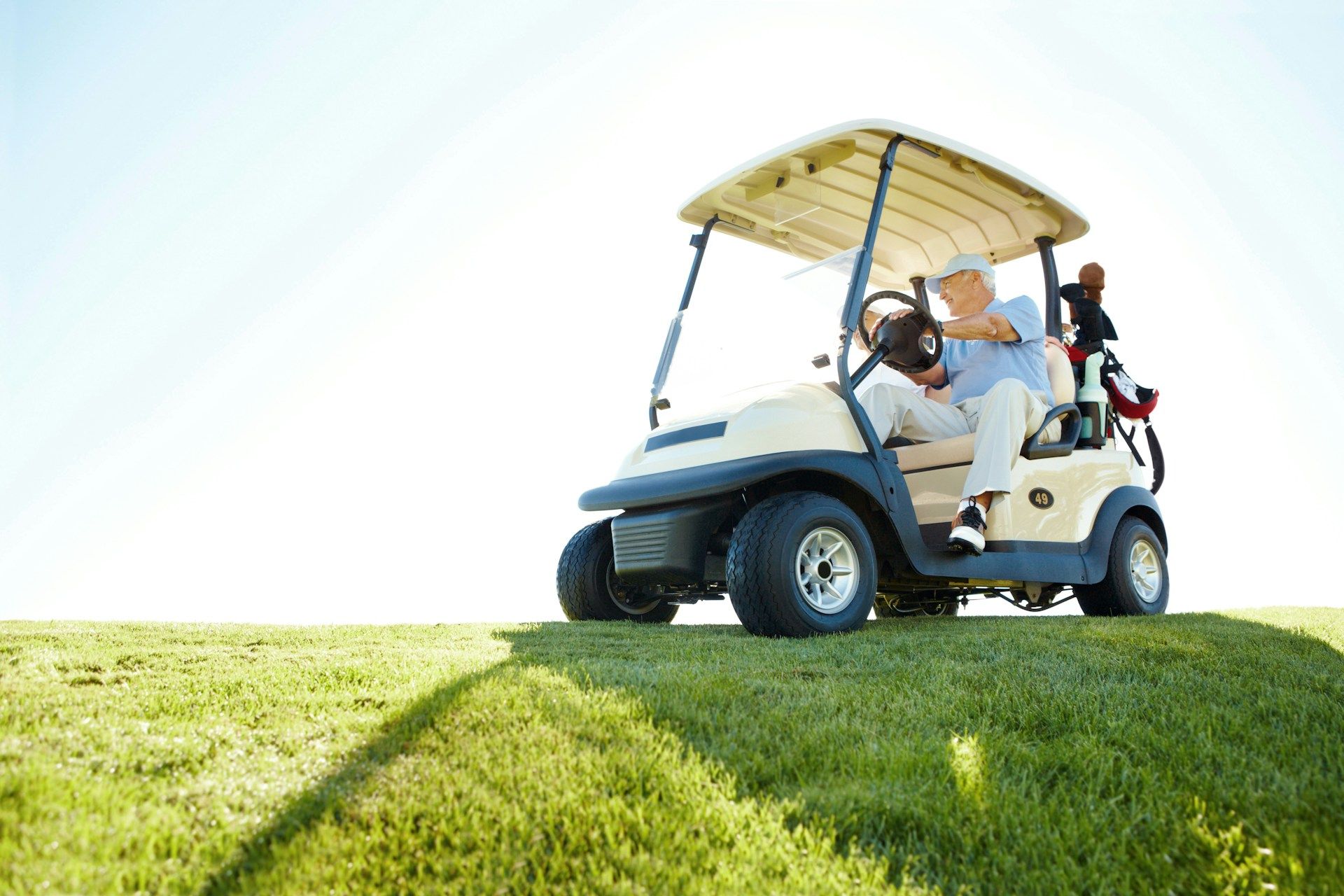 Older person in a golf cart on a grassy hill; blue sky.