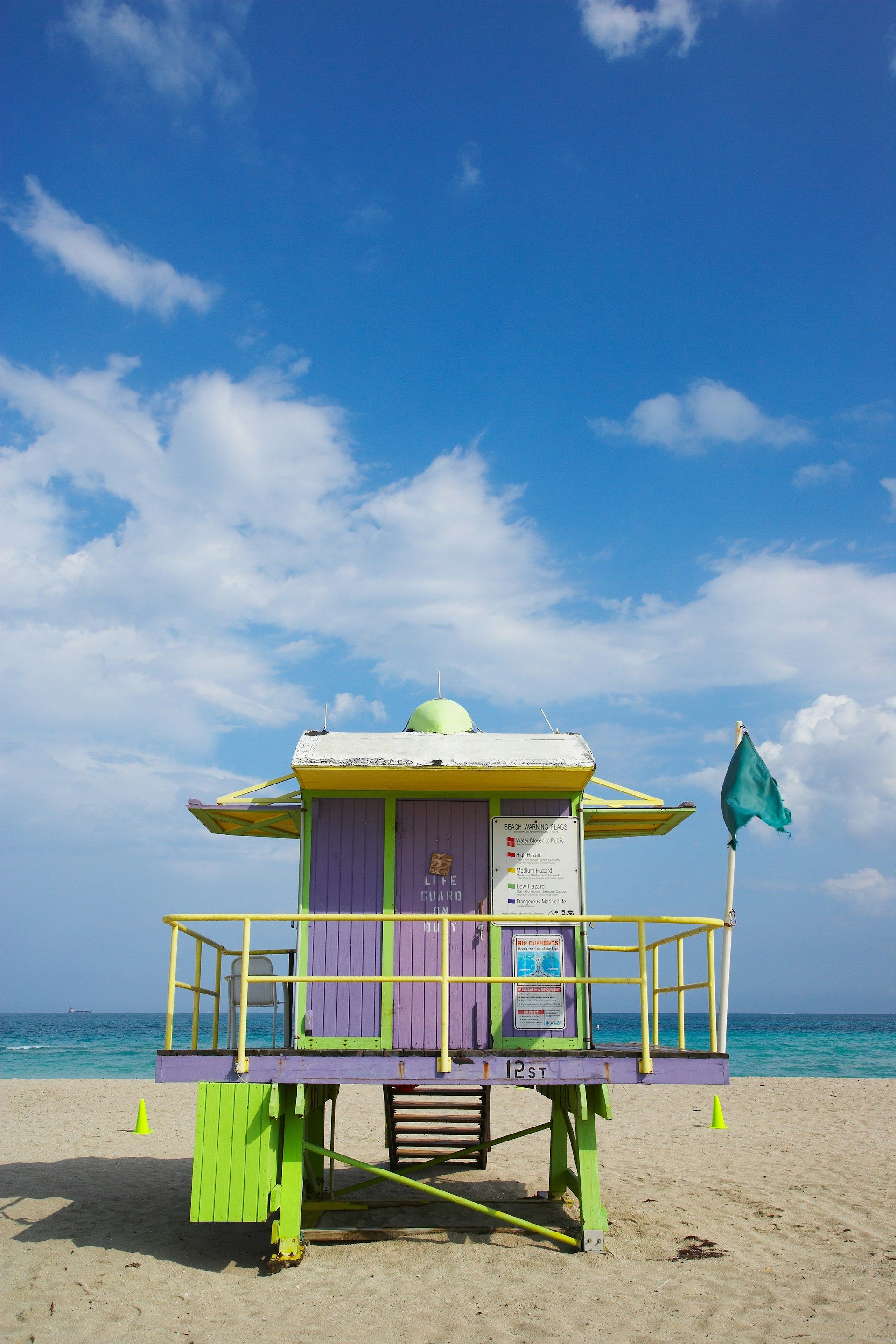 Colorful lifeguard stand on a sandy beach with blue sky and ocean in background.