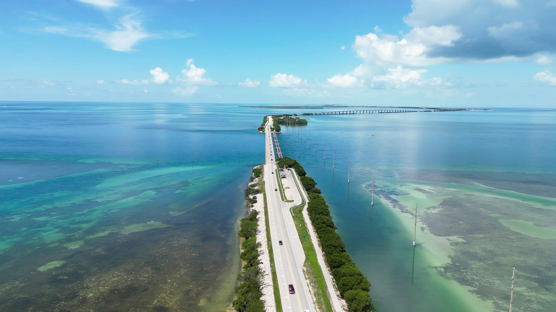 Bridge over turquoise water, connecting islands under a blue sky with clouds.