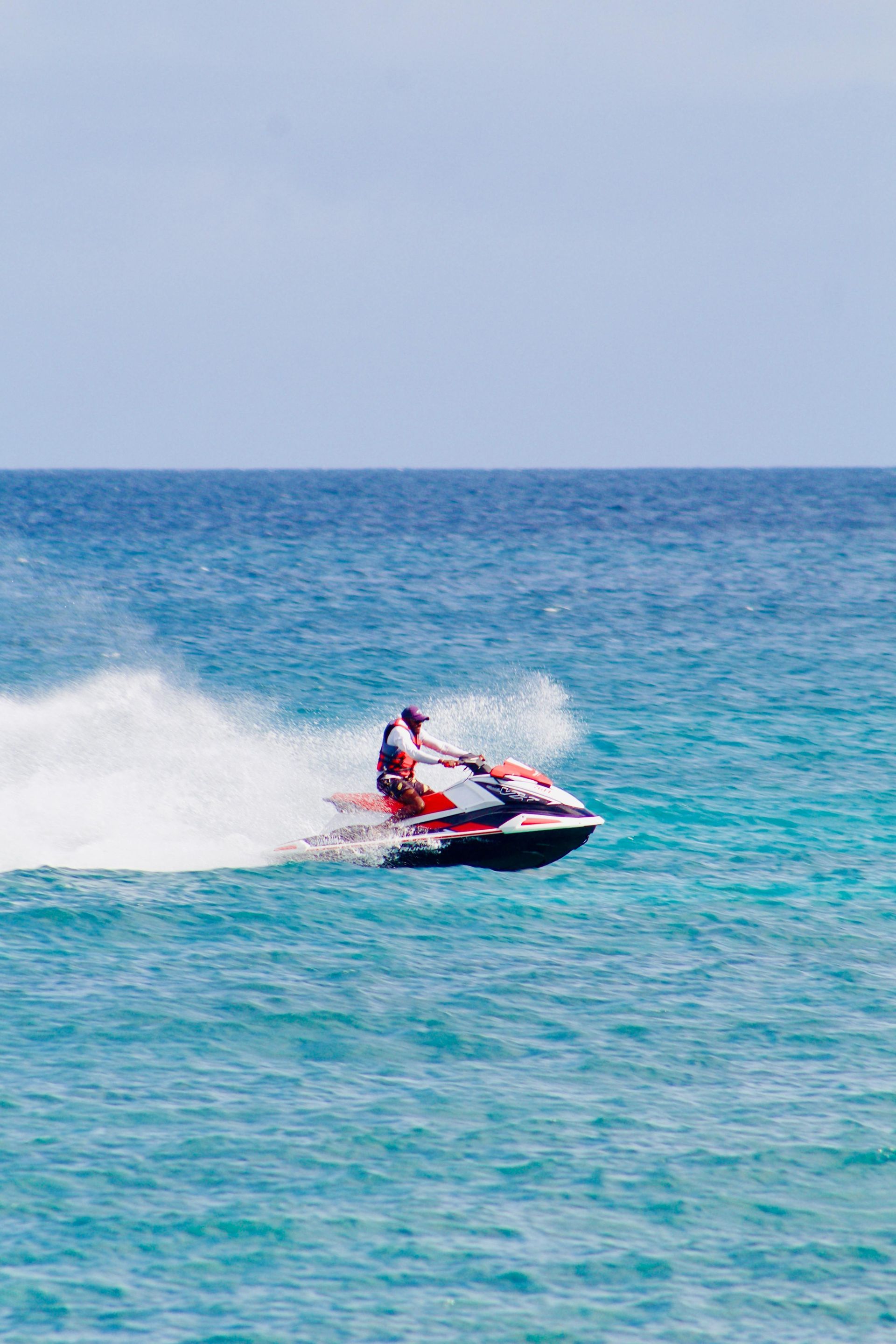 Person riding a jet ski on blue ocean, creating a white spray. Bright sunny day.