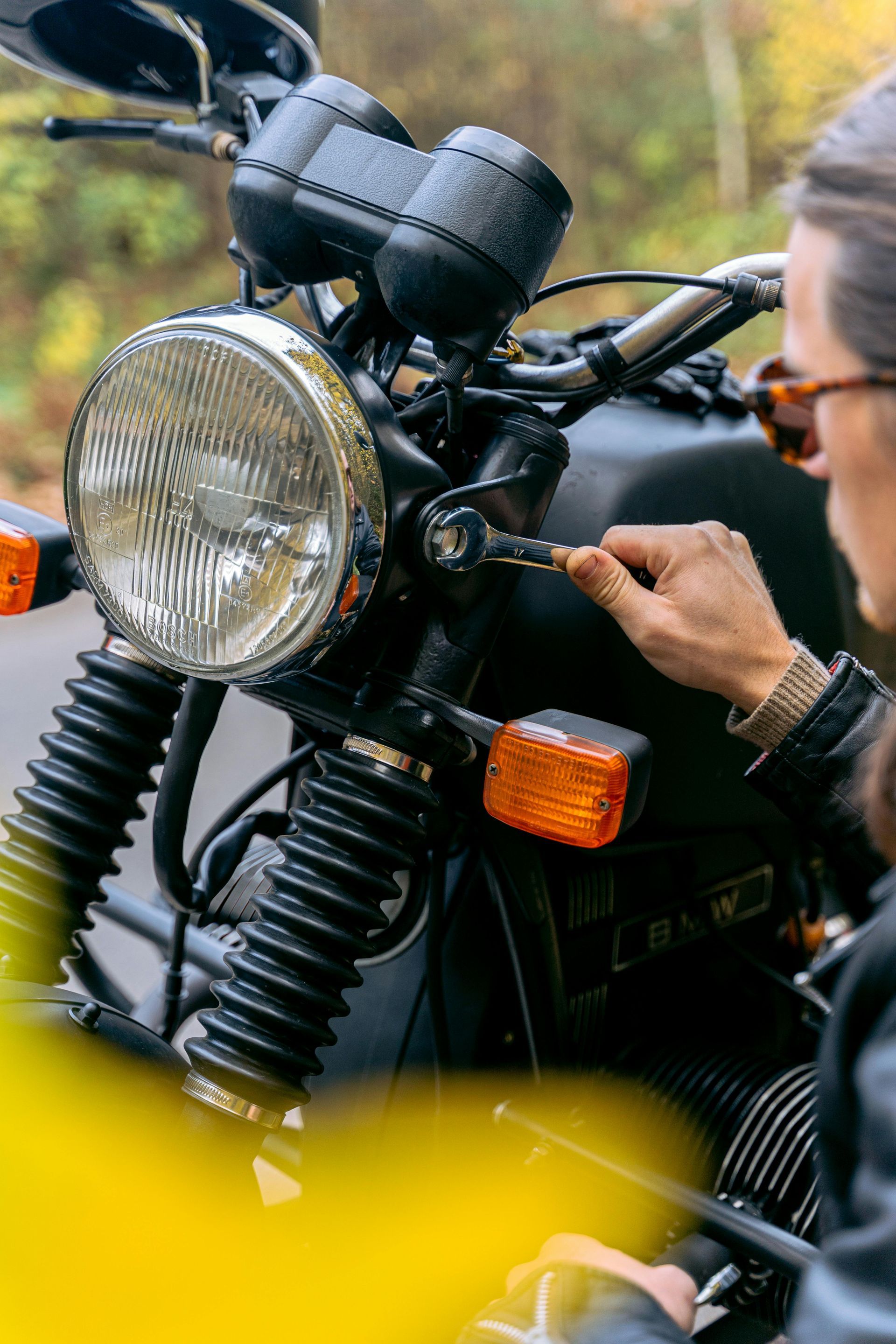 Person inserting key into black motorcycle. Autumn setting, focused on the headlight.