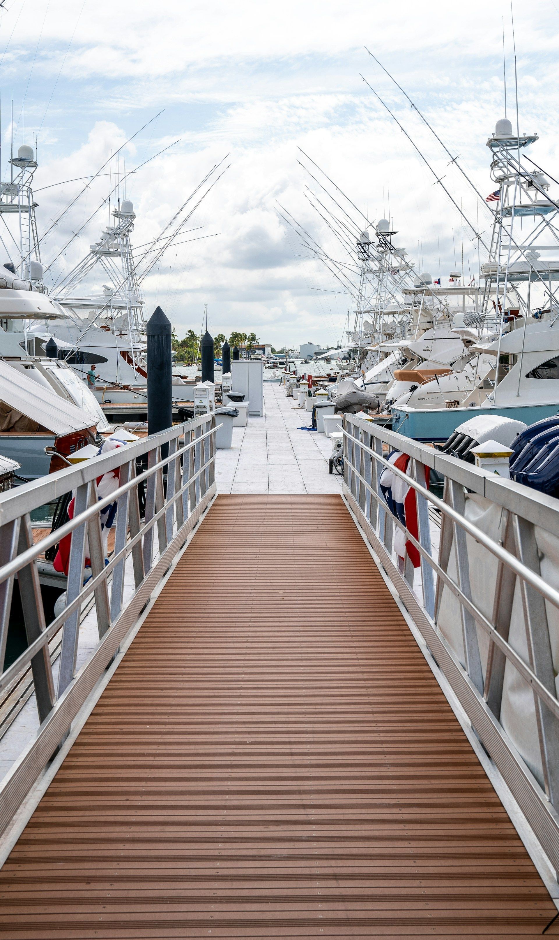 Wooden dock leading to boats docked at marina under a cloudy sky.