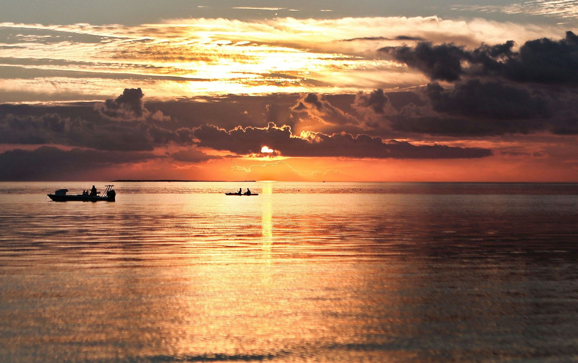 Sunset over water with two boats silhouetted; orange and gold sky with reflections.