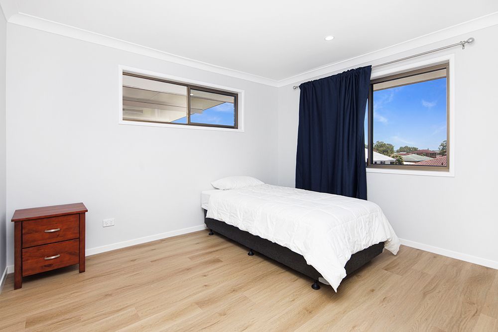 A bedroom with a single bed , nightstand , and window.