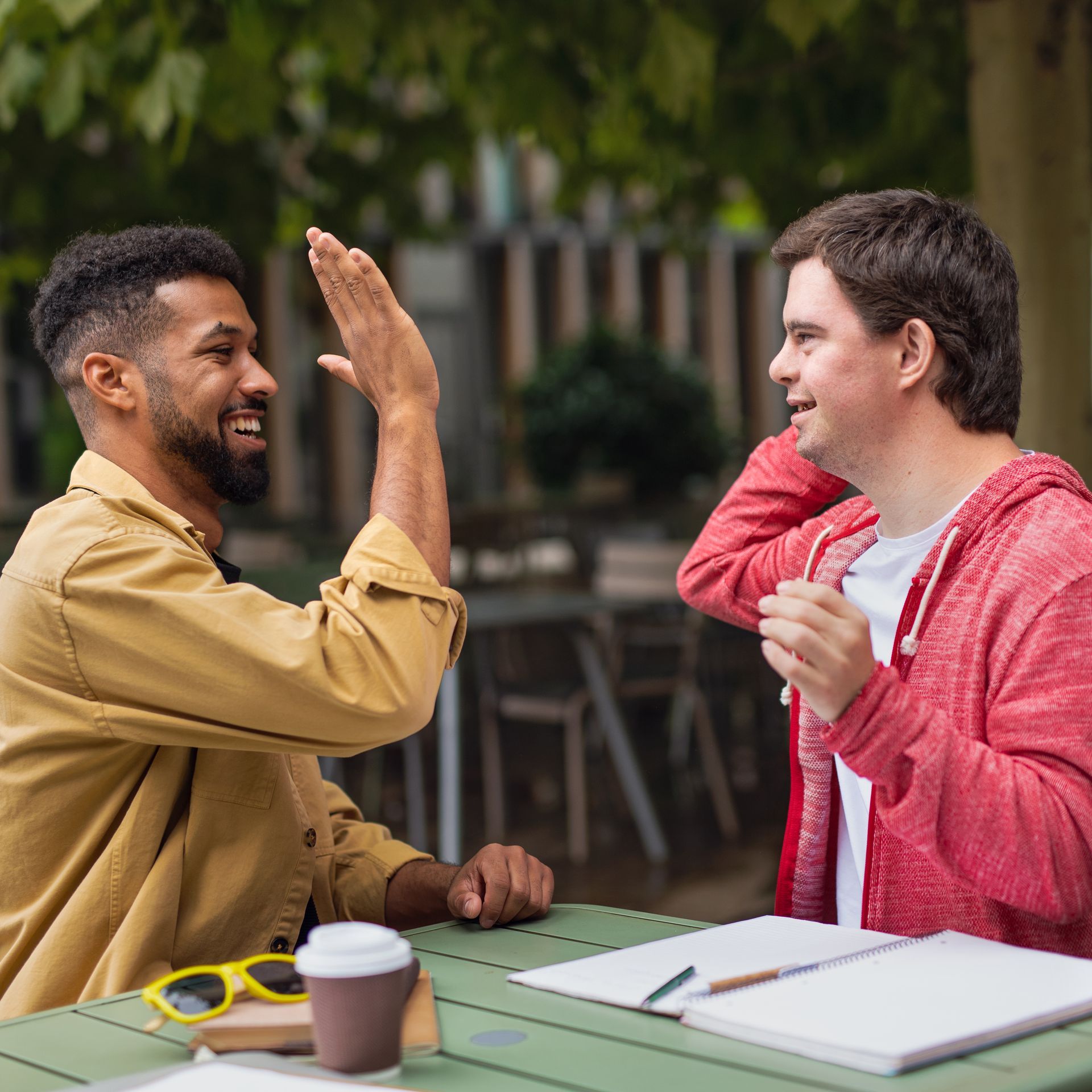 Two men are sitting at a table giving each other a high five.