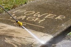 A power washer sprays a concrete surface, revealing the words 
