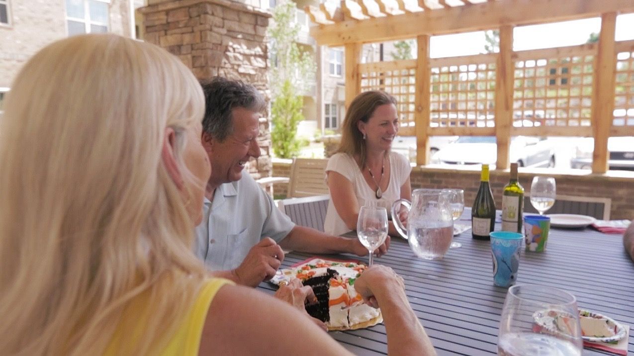 Group of adults seated at an outdoor patio table, sharing cake and drinks.
