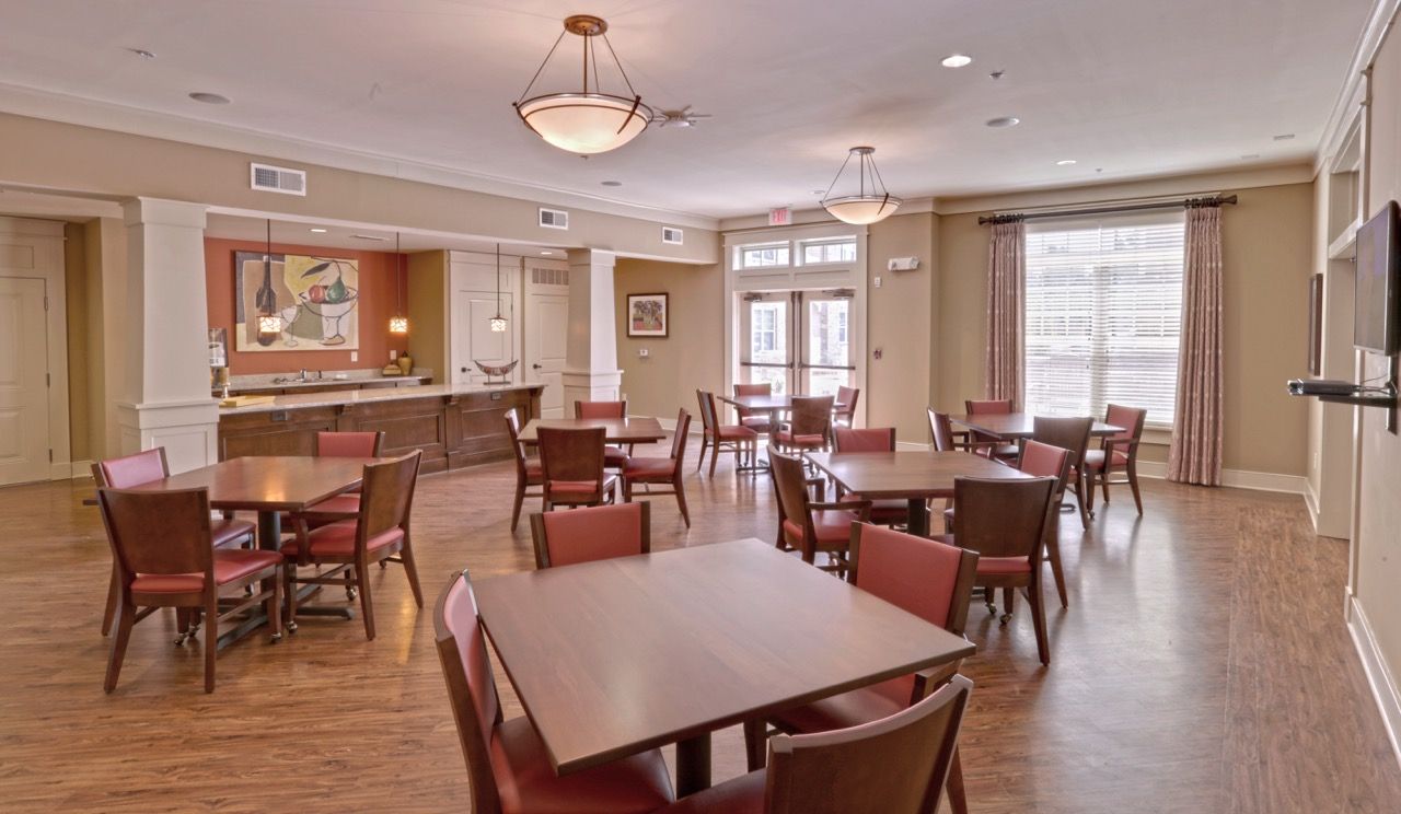 Spacious apartment community lounge with several tables, chairs, and a bar area.