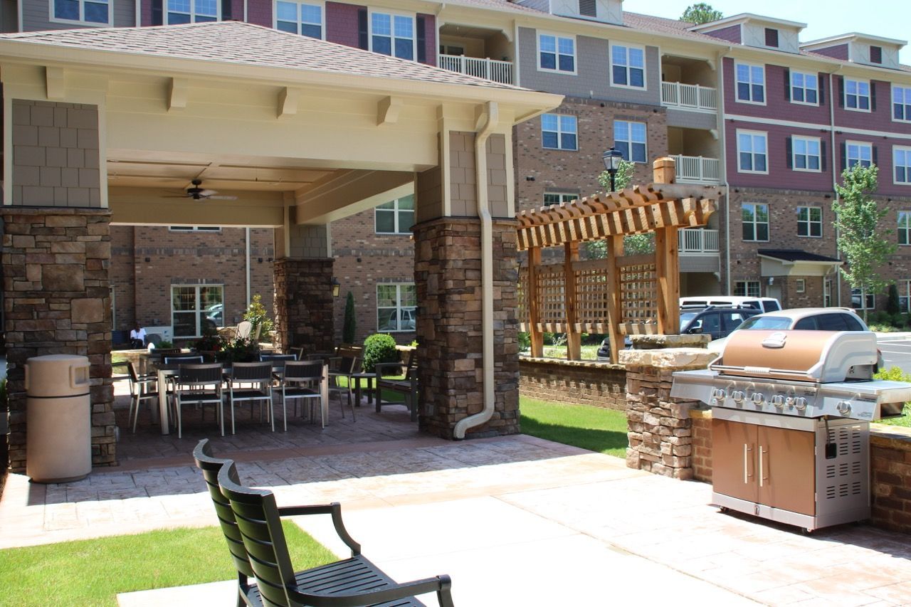 Outdoor communal seating area with a grill, pergola, and surrounding apartment buildings.