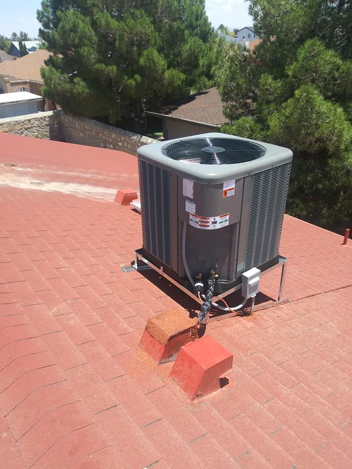 Air conditioning unit on a red rooftop, with trees in the background under a bright, sunny sky.