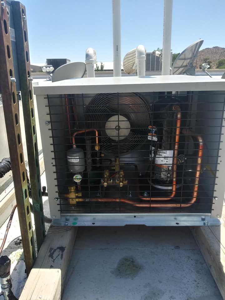 Rooftop air conditioning unit with copper piping, a fan, and a compressor visible behind a protective metal grid.