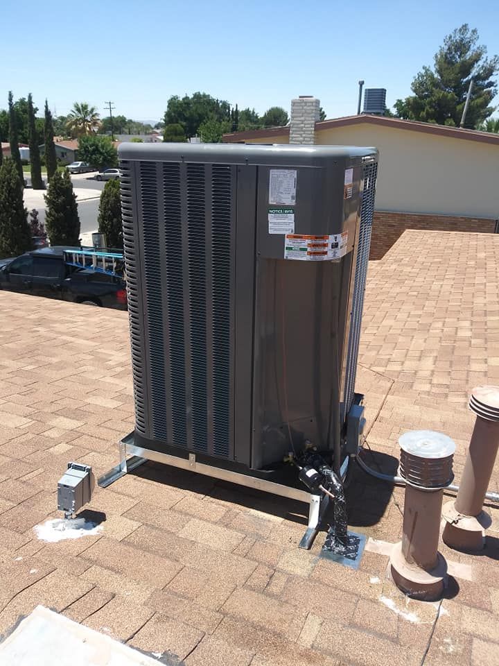 Gray air conditioning unit on rooftop, supported by metal frame, under a sunny sky.
