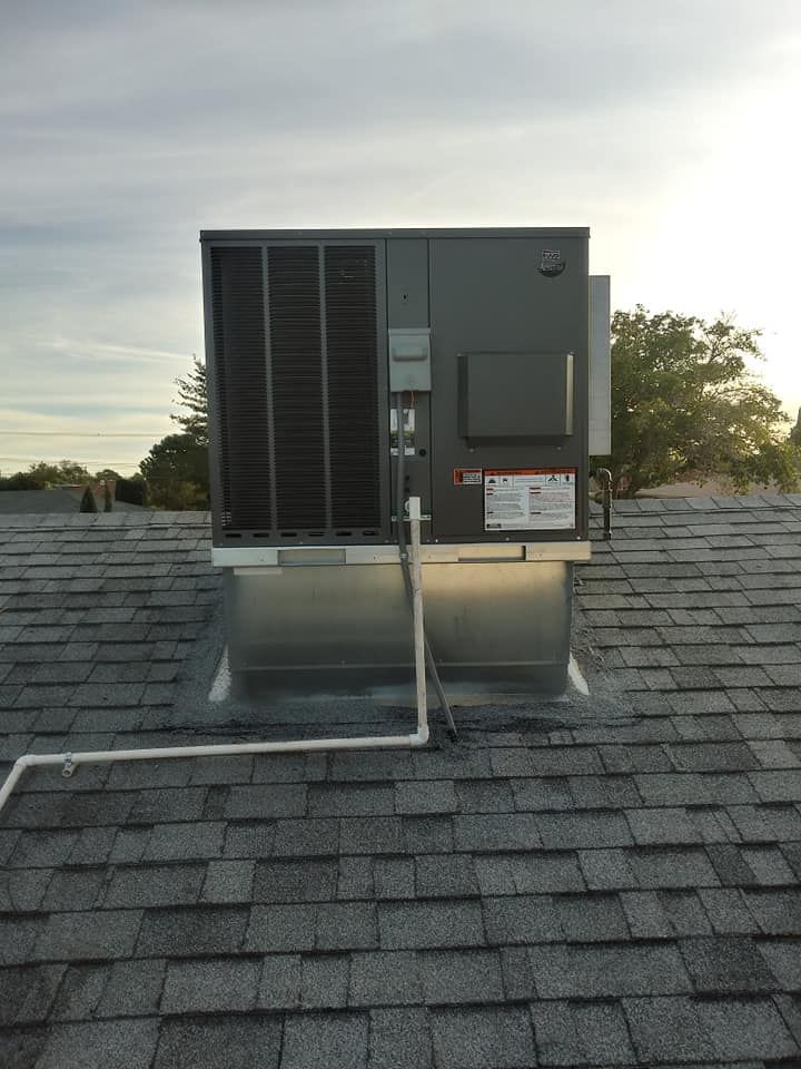HVAC unit on a gray shingled roof, silver metal platform, white pipe runs to the left, sky background.