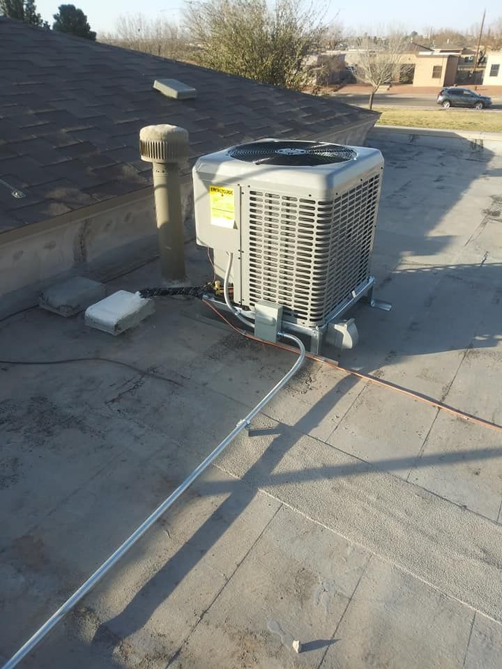 Air conditioning unit on a flat roof. Metal conduit and vent pipe are present. Sunny day.
