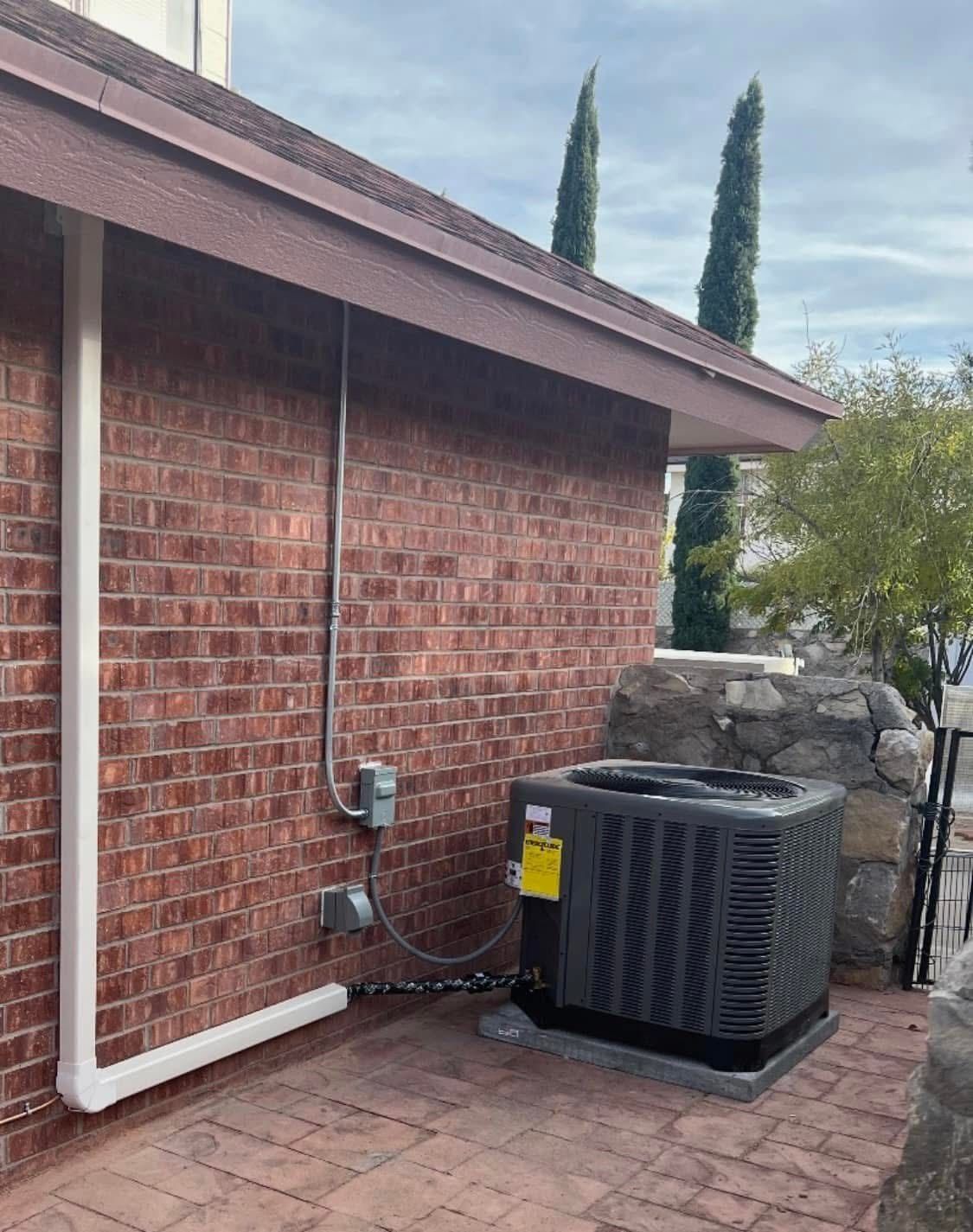 Brick building exterior with AC unit, electrical box, and white conduit. Brown roof, two trees visible.