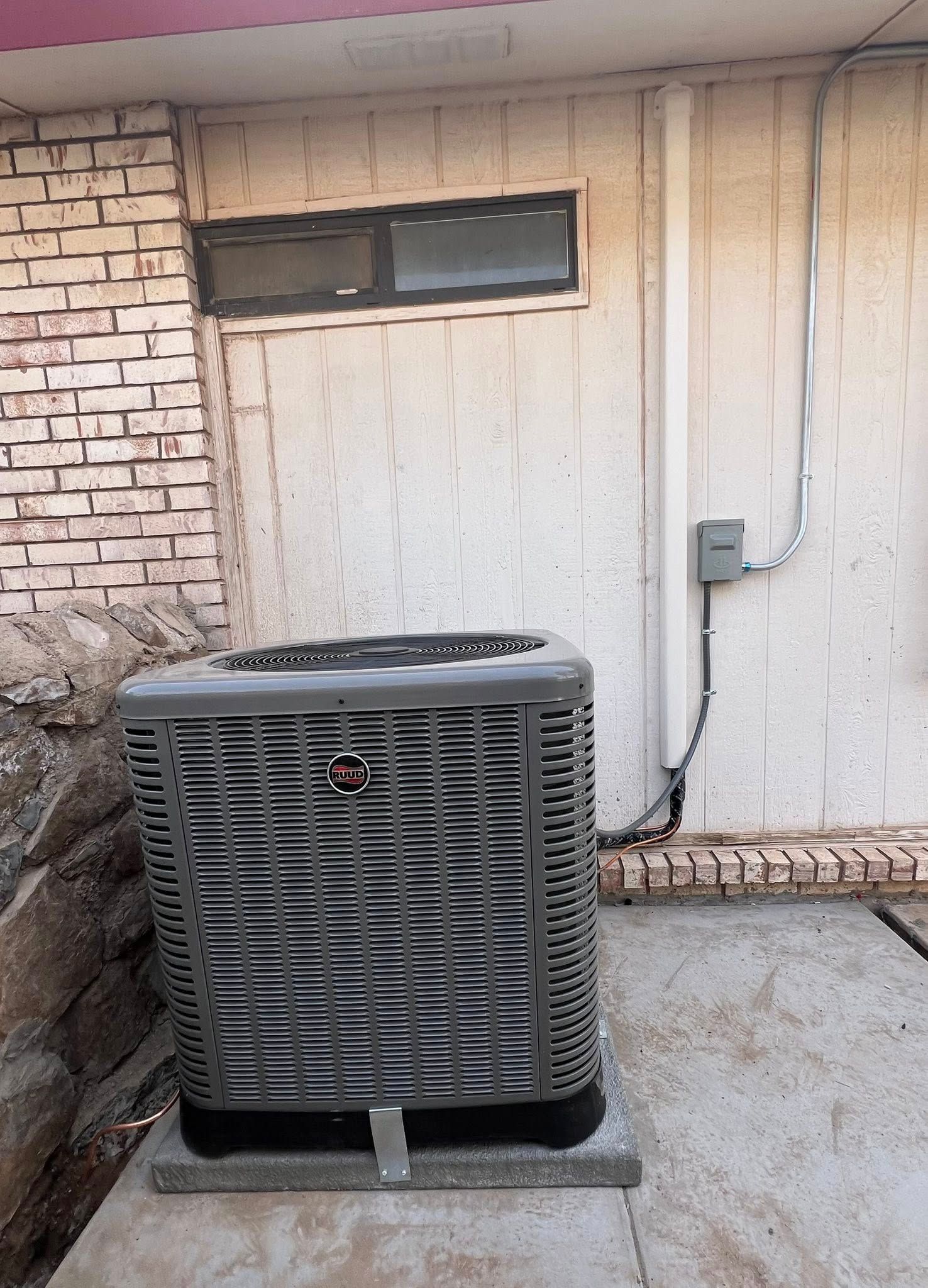 Air conditioning unit outside a building with brick and stucco walls, electrical components.