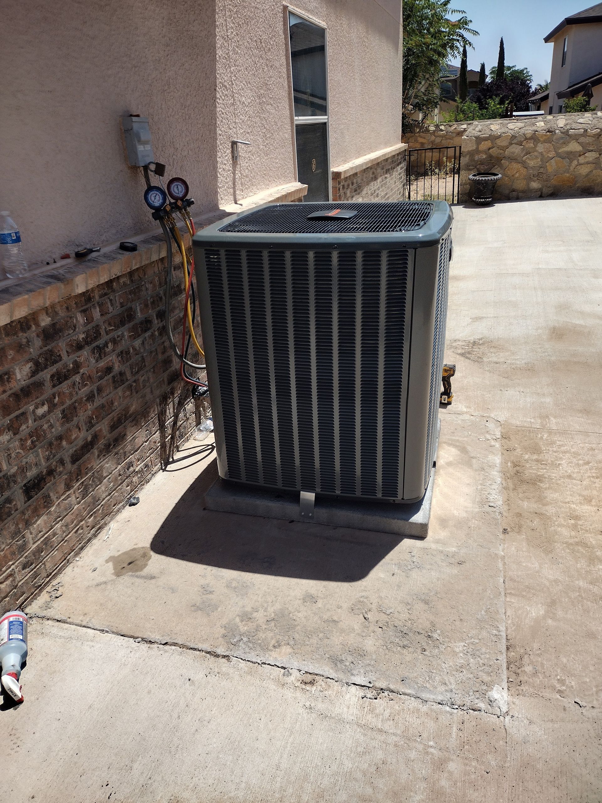 Air conditioning unit outside a building, gauge attached. Concrete patio. Sunny day.
