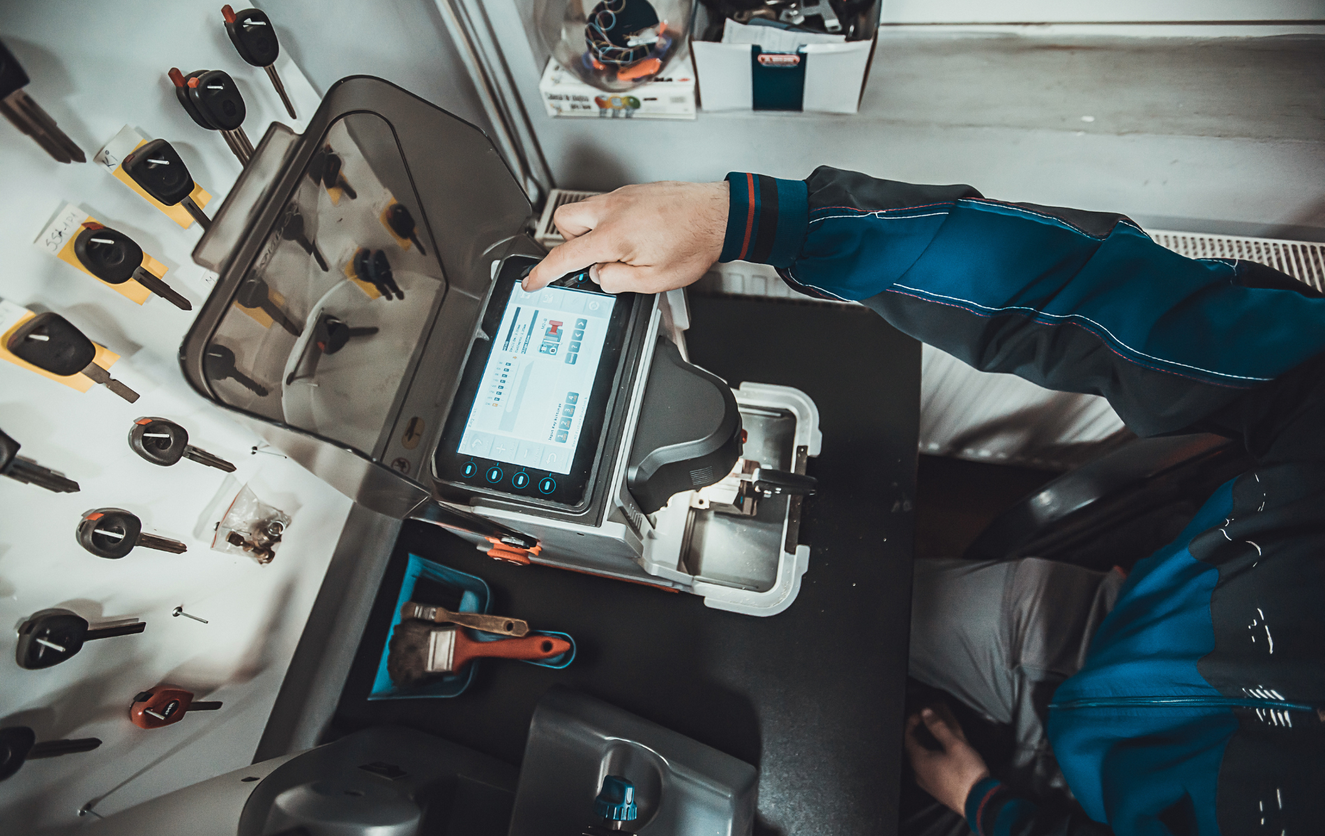 A man is sitting at a desk using a machine to make keys.