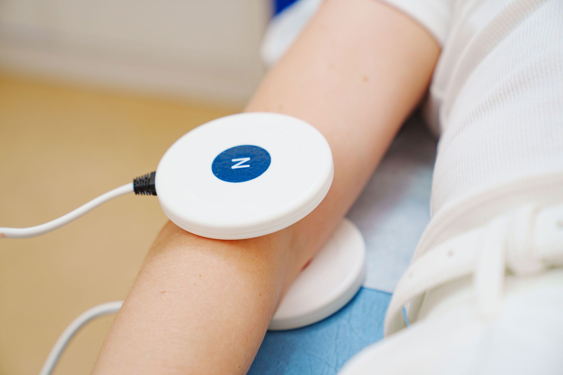 Person's arm with two white circular devices attached, likely for medical treatment. The devices are connected by wires.