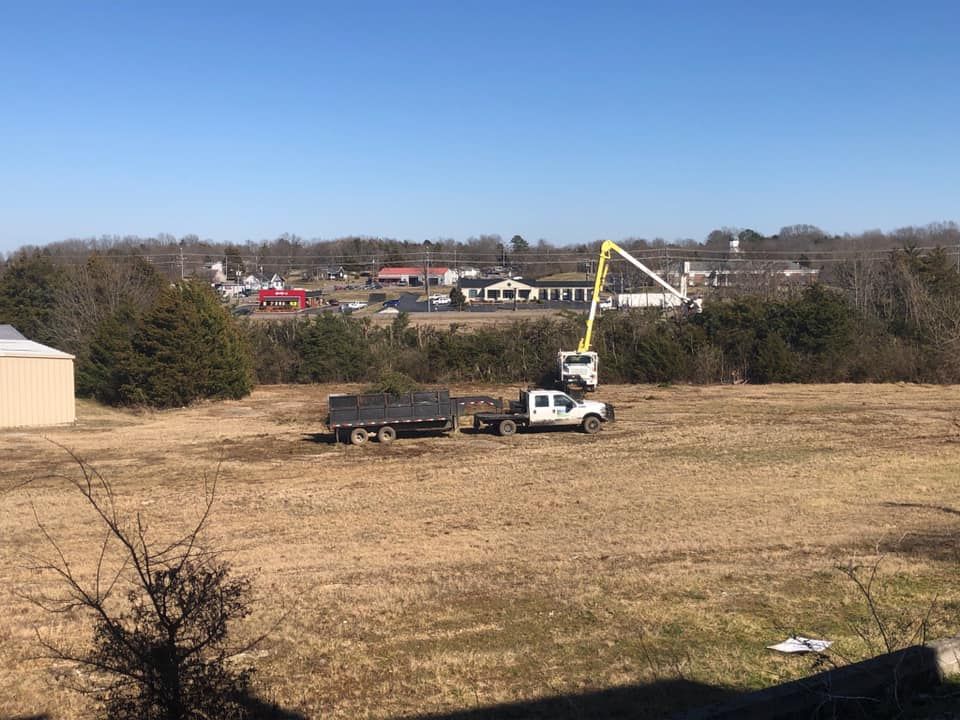 White utility truck with boom lift in a dry field, with houses and trees in the background.