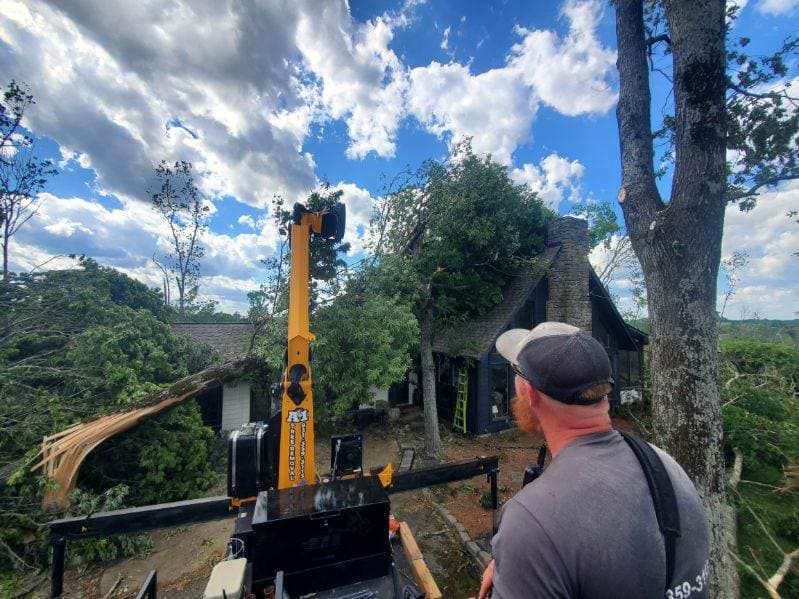Worker operating yellow excavator near a rural house under a cloudy blue sky