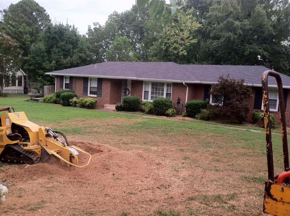 Brick house with a grassy yard, trees, and yellow construction equipment in the foreground