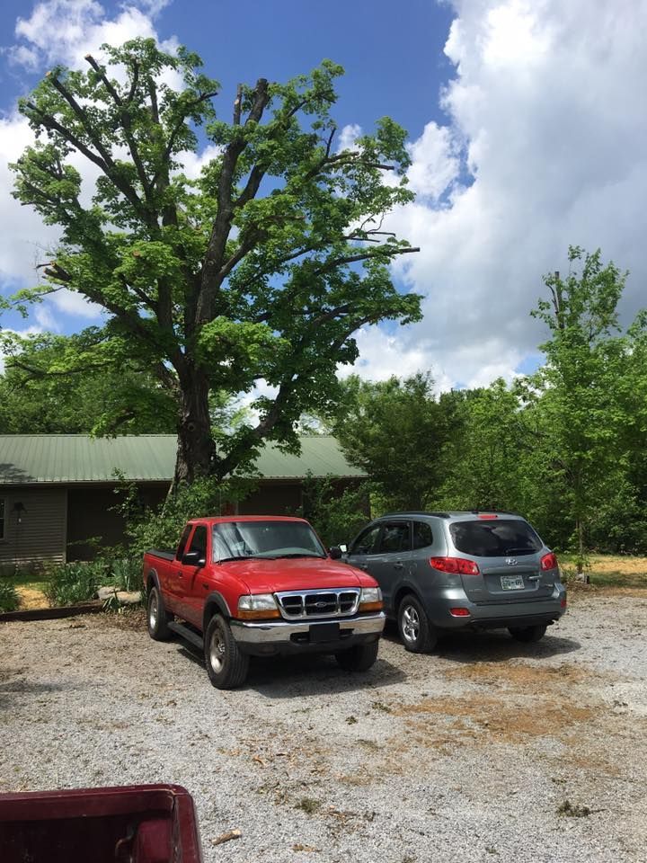 Red pickup and gray SUV parked on a gravel lot beside a building and large tree