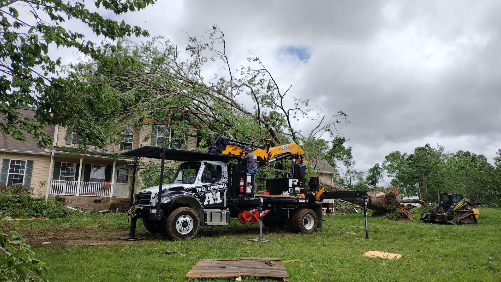 White utility truck with a yellow crane parked on a grassy lot beside a house under cloudy skies