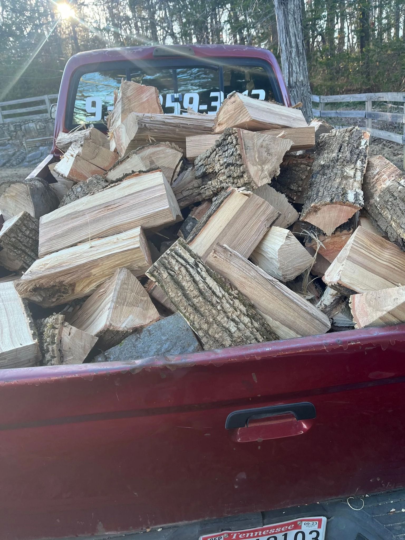 Pickup truck bed piled high with split firewood logs in a wooded area