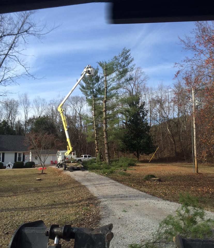 A concrete pump truck extends a long yellow boom over a driveway beside a house and trees.