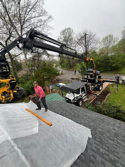 Rain-soaked workers moving equipment around a tree trimming truck with a crane arm in a wooded area