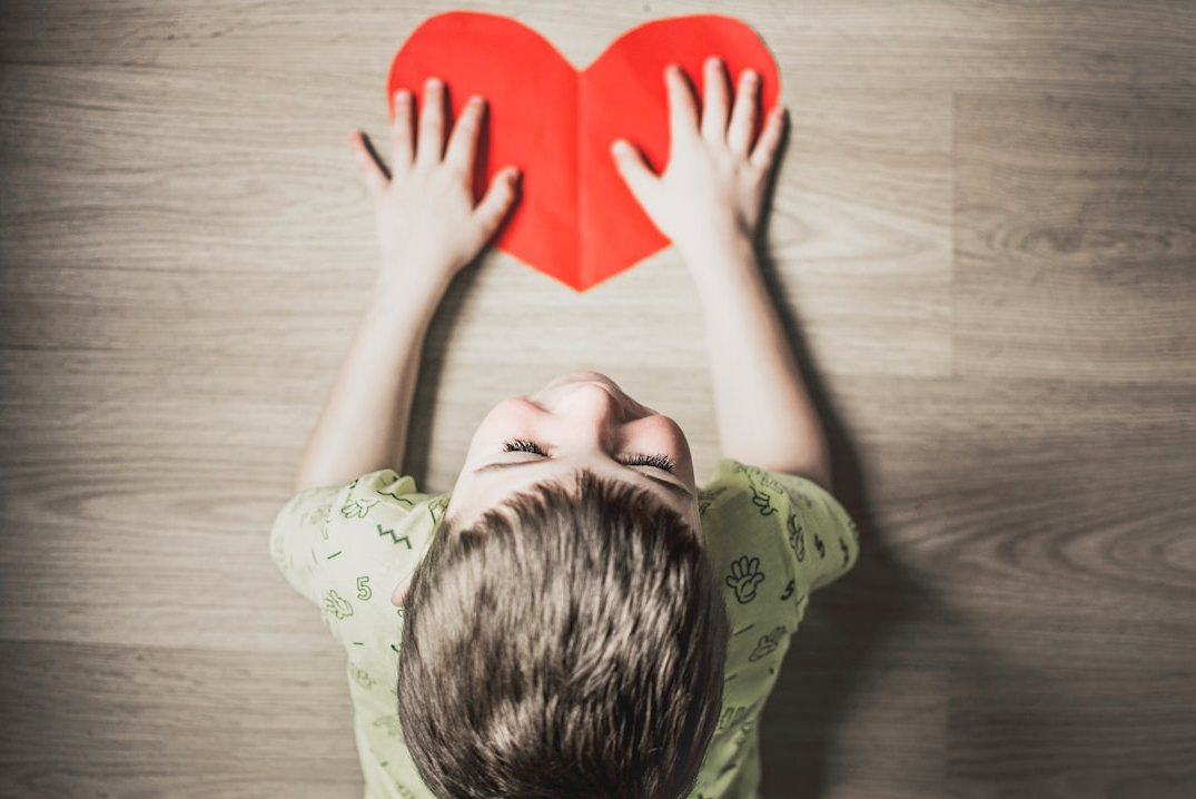 A young boy is holding a red paper heart in his hands.