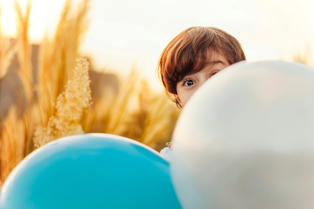 A young boy is holding two balloons in a field.