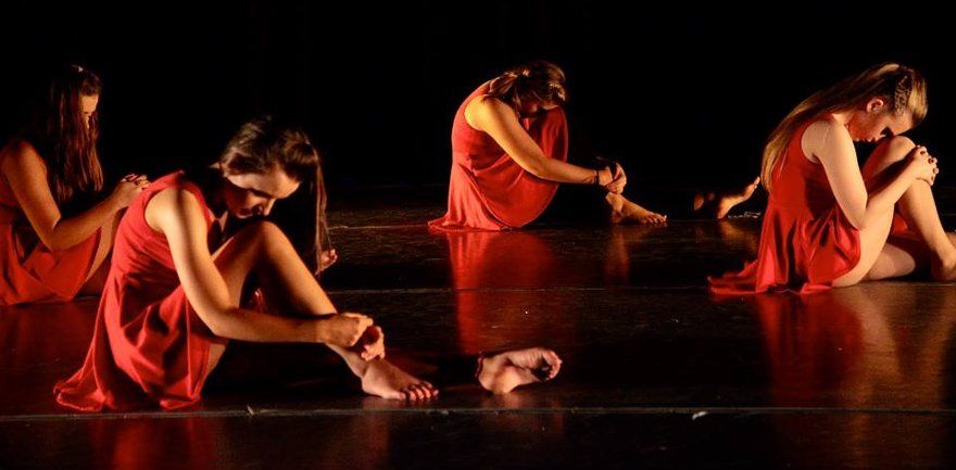 dancers in red dresses on stage in dramatic shadow