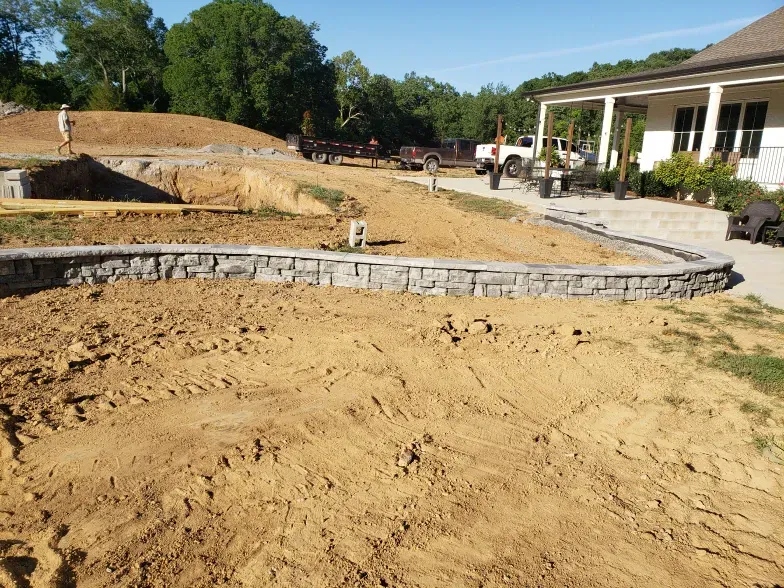 A stone wall is being built in the dirt in front of a house.
