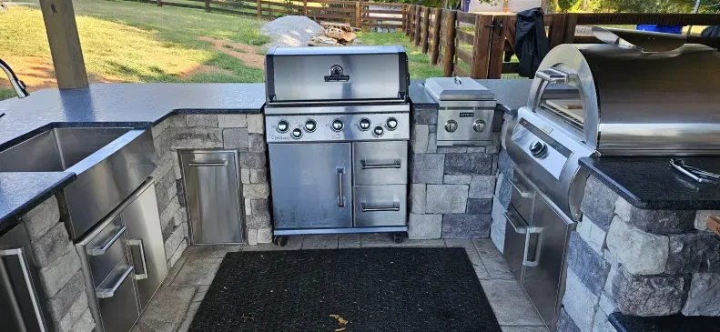 A stainless steel grill is sitting next to a sink in an outdoor kitchen.