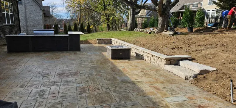 A patio with a grill and a fire pit in the backyard of a house.