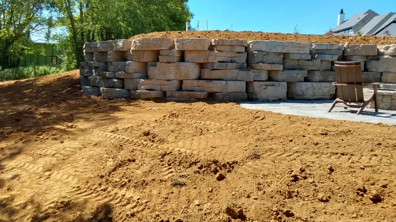 A large stone wall is sitting in the middle of a dirt field.