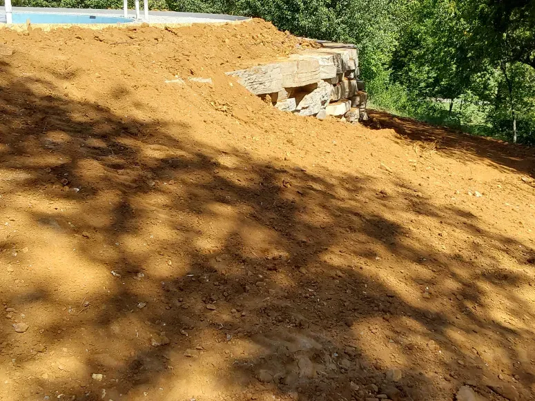 A pile of dirt is sitting on top of a hill next to a pool.