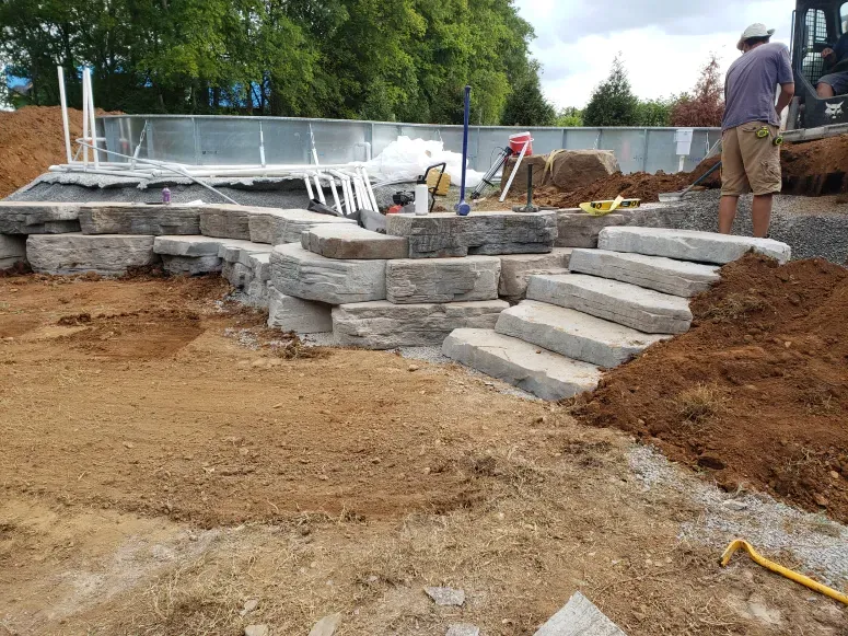 A man is standing in the dirt in front of a swimming pool being built.