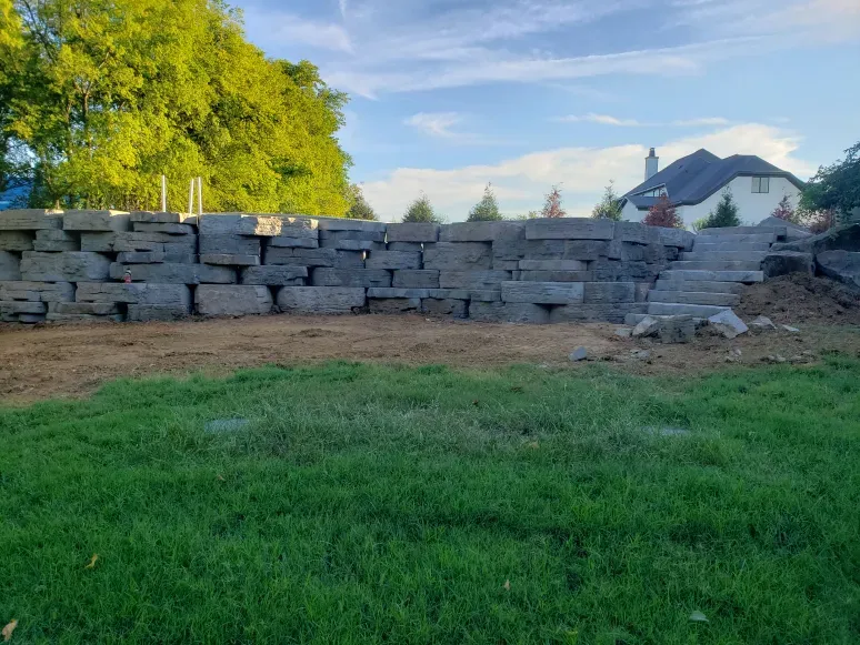 A large stone wall is sitting in the middle of a lush green field.