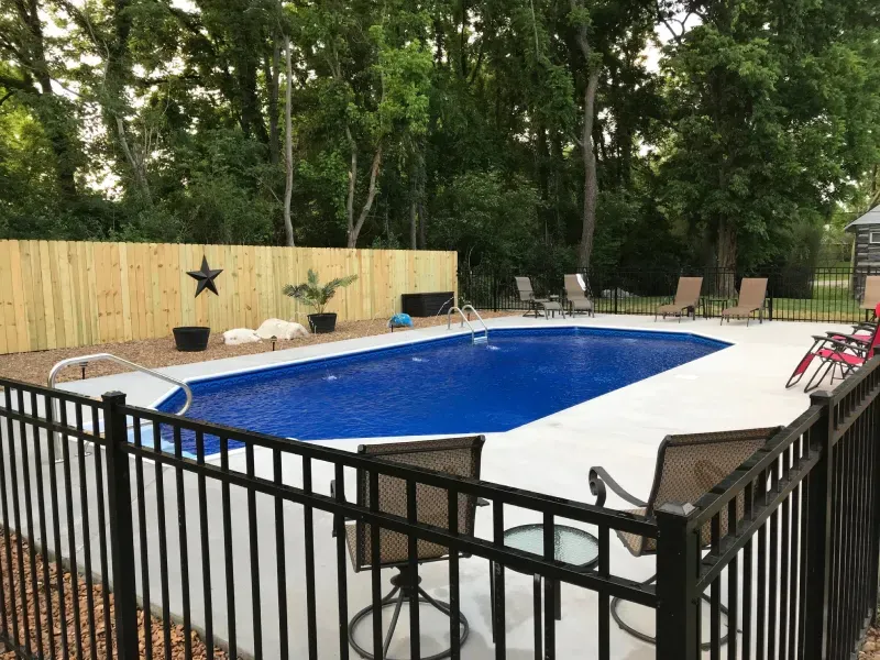 A large swimming pool surrounded by a black fence and chairs.