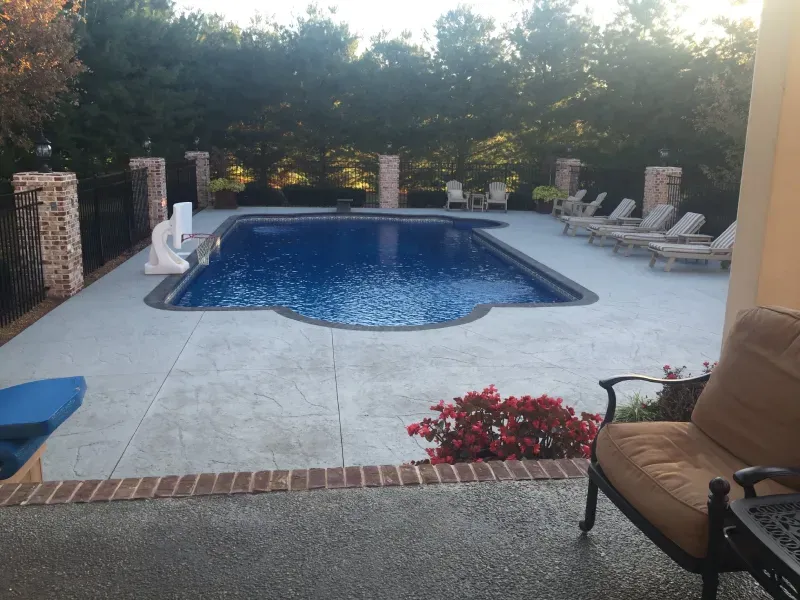 A large swimming pool is surrounded by chairs and a bench
