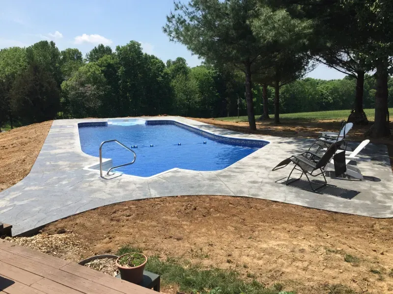 A large blue swimming pool is surrounded by trees and a deck.