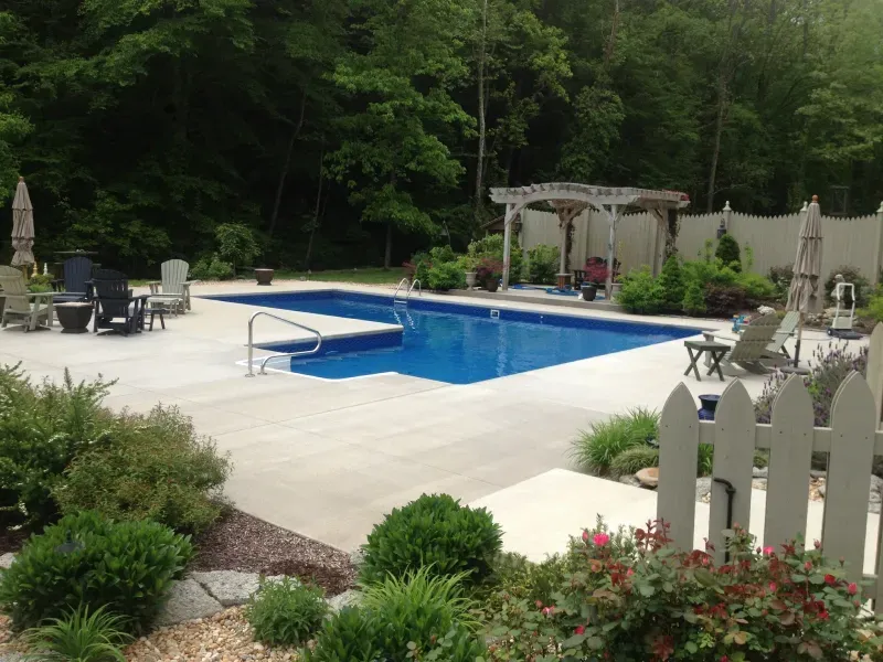 A large swimming pool is surrounded by a white picket fence and chairs.