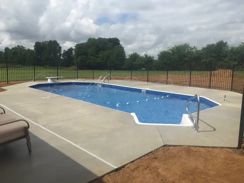 A large swimming pool is surrounded by a fence in a backyard.