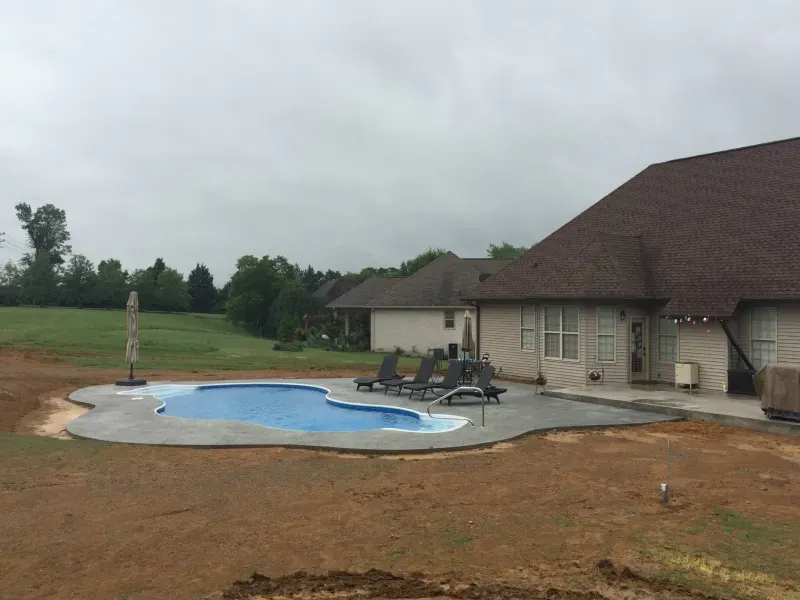 A large swimming pool is in the backyard of a house.
